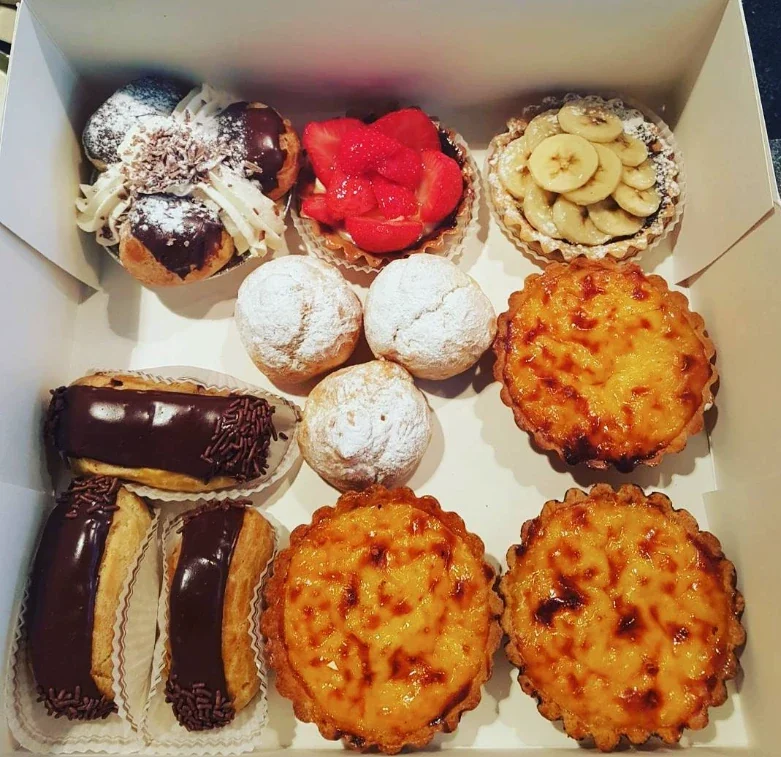 Doos met gebak: eclairs, aardbeientaartjes, een bananentaartje, roomsoesjes en vlaaitjes