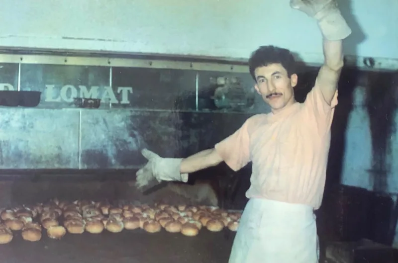 Oude foto: een bakker met ovenhandschoenen toont een plaat verse broodjes