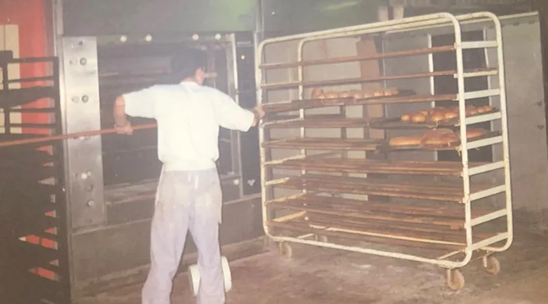 Oude foto: een bakker trekt een rek met broden bij de oven