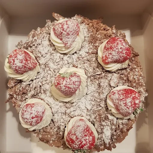 Taart met slagroom, aardbeien, chocoladeschilfers en poedersuiker in een taartdoos